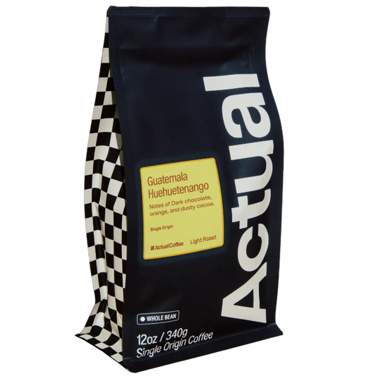 A 12 oz bag of Actual Coffee's Guatemala Huuetenango single origin coffee. The bag is dark navy blue with a large white vertical 'Actual' logo, a yellow label, and a black-and-white checkered pattern on the left side.