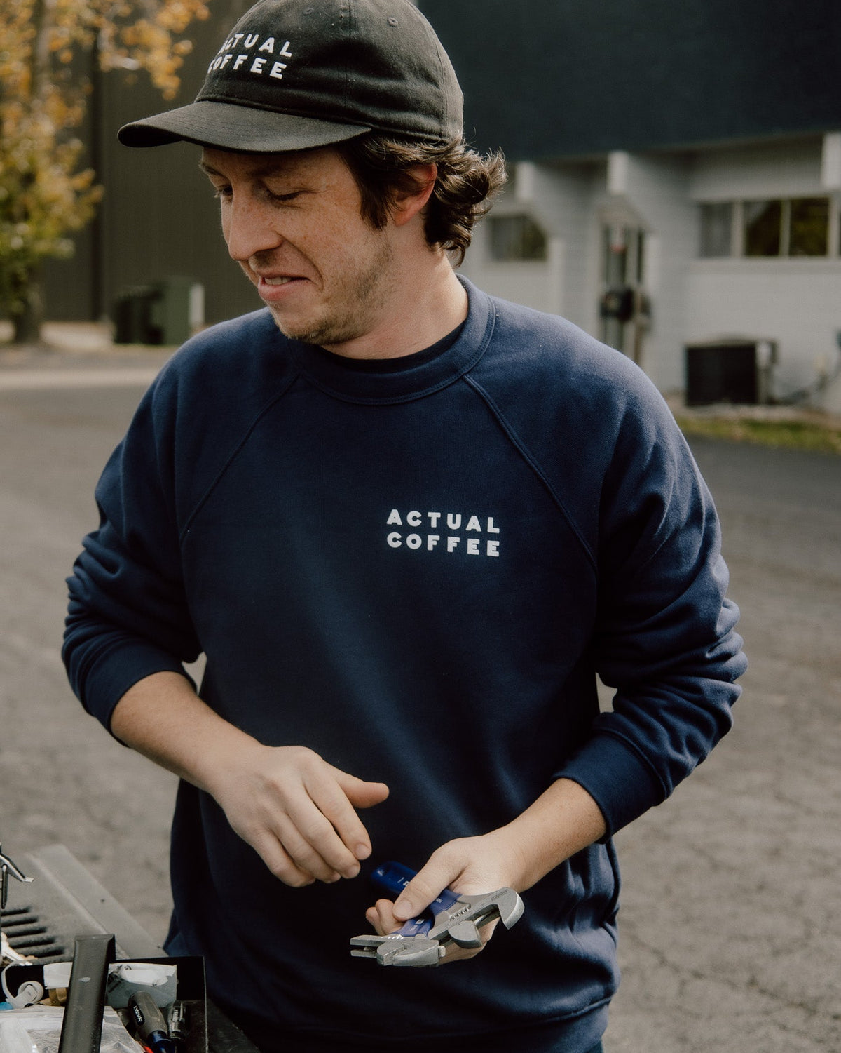 Man wearing an 'Actual Coffee' sweatshirt and cap, standing outdoors.