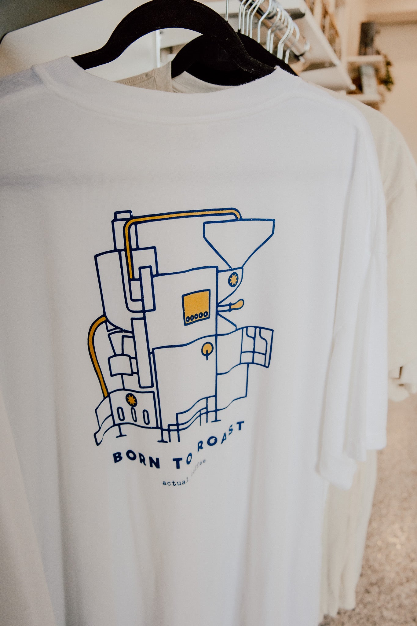 White t-shirt with a graphic design and 'Born to Roast' text on a hanger.