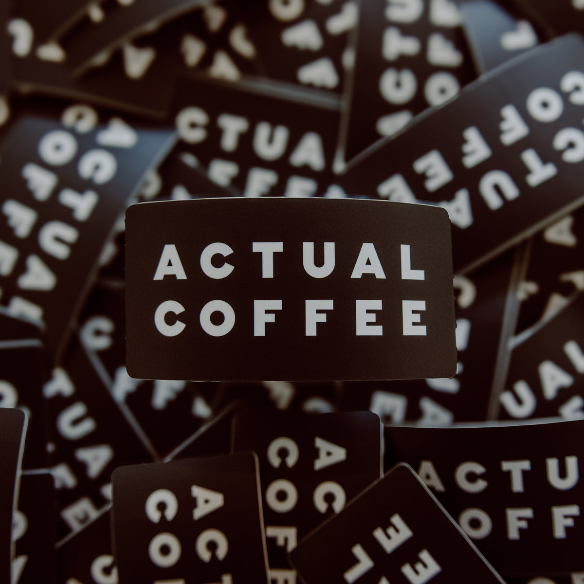 Black stickers with 'ACTUAL COFFEE' text on a background of similar stickers.