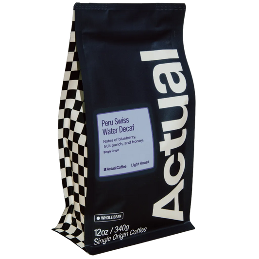 A 12 oz bag of Actual Coffee Peru Swiss Water Decaf whole bean single origin coffee. The bag is black with a large white vertical 'Actual' logo, a light blue label, and a black-and-white checkered pattern on the left side, shown on a plain white background.