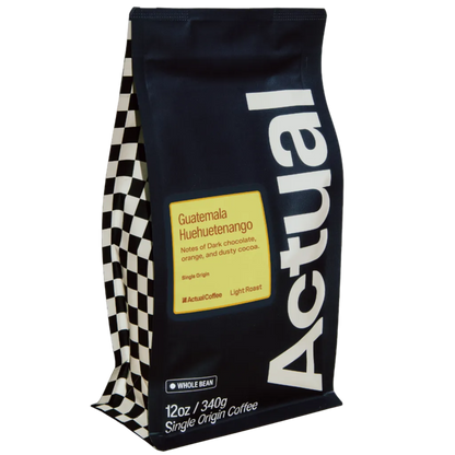 A 12 oz bag of Actual Coffee's Guatemala Huuetenango single origin coffee. The bag is dark navy blue with a large white vertical 'Actual' logo, a yellow label, and a black-and-white checkered pattern on the left side.