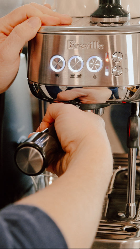 Person using a Breville espresso machine with hands on the handle and control panel.