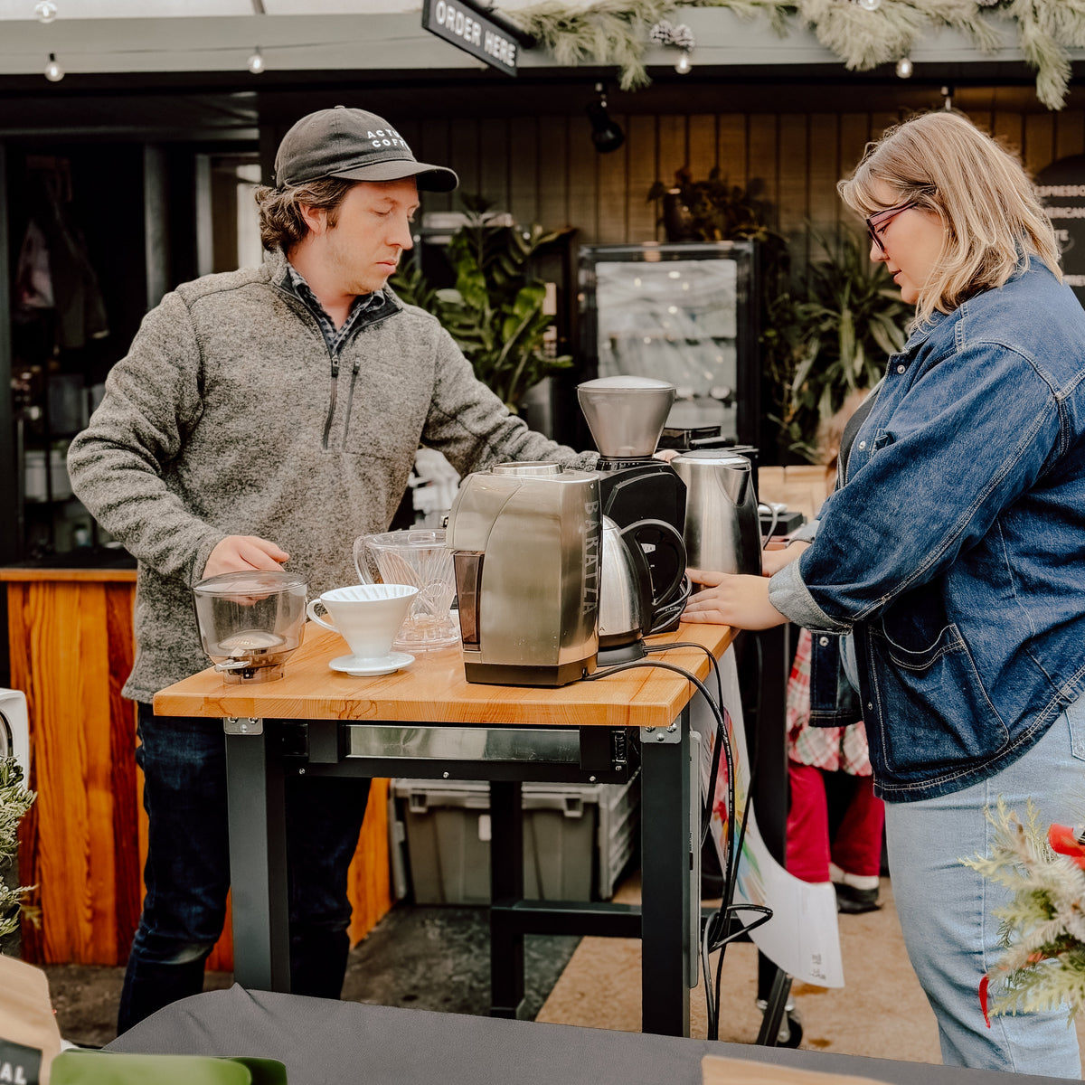 Person making coffee at a counter with another person observing.